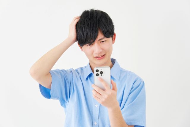 携帯を見ながら頭に手を置いて悩む男性